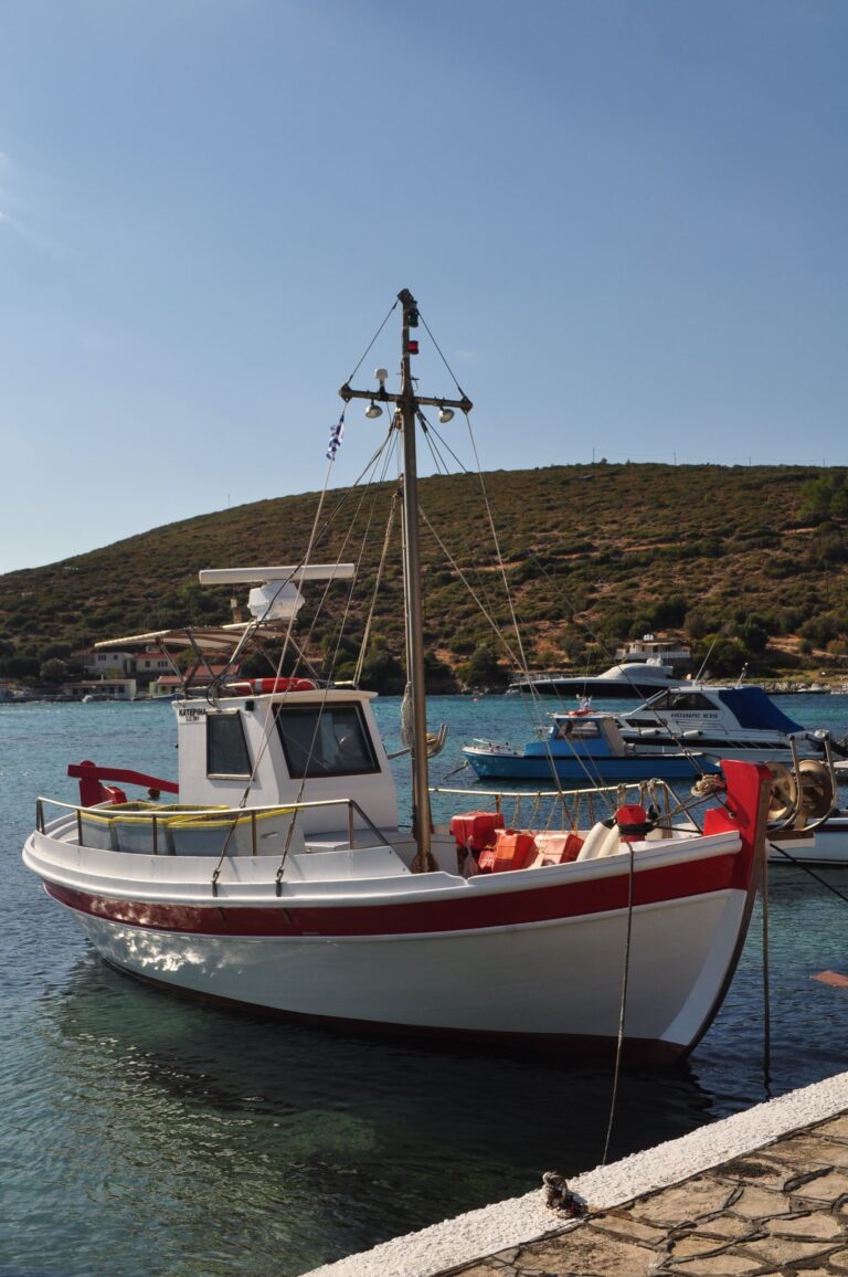 A fishing boat moored in the calm waters of Samos Harbor, Greece, with hills in the background under a clear sky.